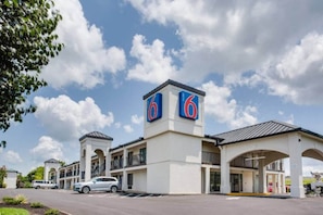Un motel con un llamativo letrero con el número '6', varios balcones y un estacionamiento.