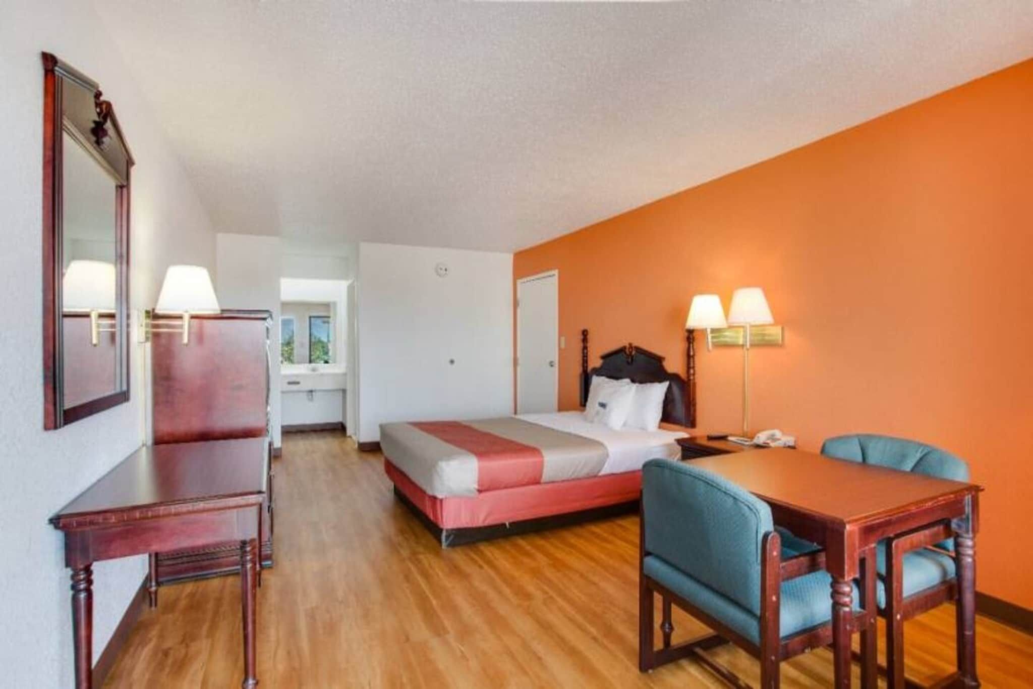 Quarto de hotel com cama, escrivaninha, cadeira e mesa. Há uma janela e uma porta.