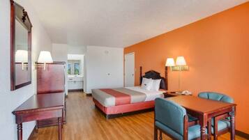 Quarto de hotel com cama, escrivaninha, cadeira e mesa. Há uma janela e uma porta.