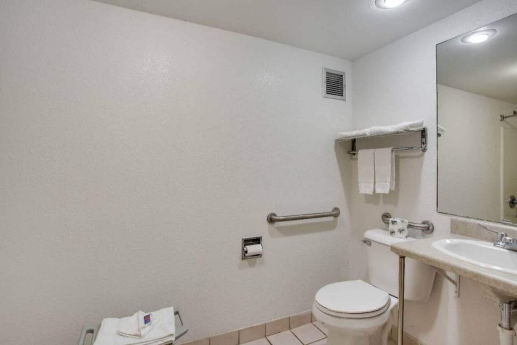 A standard bathroom with a toilet, sink, mirror, and towel rack.