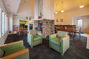 Eine Lobby mit Sitzgelegenheiten, einem Steinkamin und einem Essbereich mit Tischen und Stühlen.