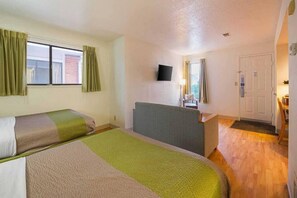Ein Hotelzimmer mit zwei Betten, einem Schreibtisch, einem Sessel, einem Fernseher und einer Tür.