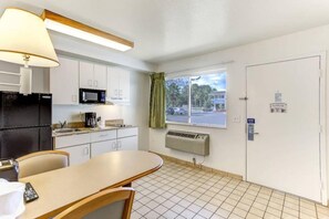 A compact kitchen with a microwave, stove, and a coffee maker. There's a dining table with chairs, a window with a view of the street, and a door with a sign. - 1 Queen Bed|Micfridge,Smoking (Kissimmee)