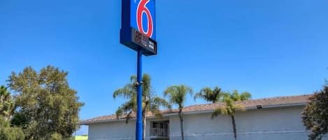 A motel sign with the number 6, a parking lot, and a building with a tiled roof.