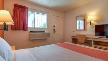 Ein Hotelzimmer mit Bett, Schreibtisch, Stuhl, Fernseher und Klimaanlage.