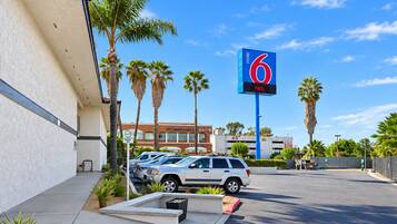 A parking lot with a 6 Motel sign, palm trees, and a building with a sign that says 'Desert Oasis.'
