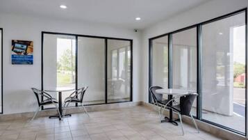 A spacious room with large windows, a tiled floor, and two tables with chairs.