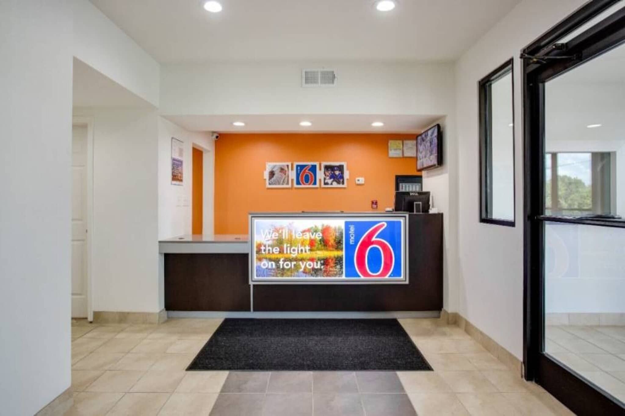 A reception area with a desk, a black mat, and a wall with framed pictures and a sign.