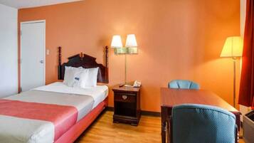 A hotel room with a bed, bedside table, lamp, chair, and a desk.