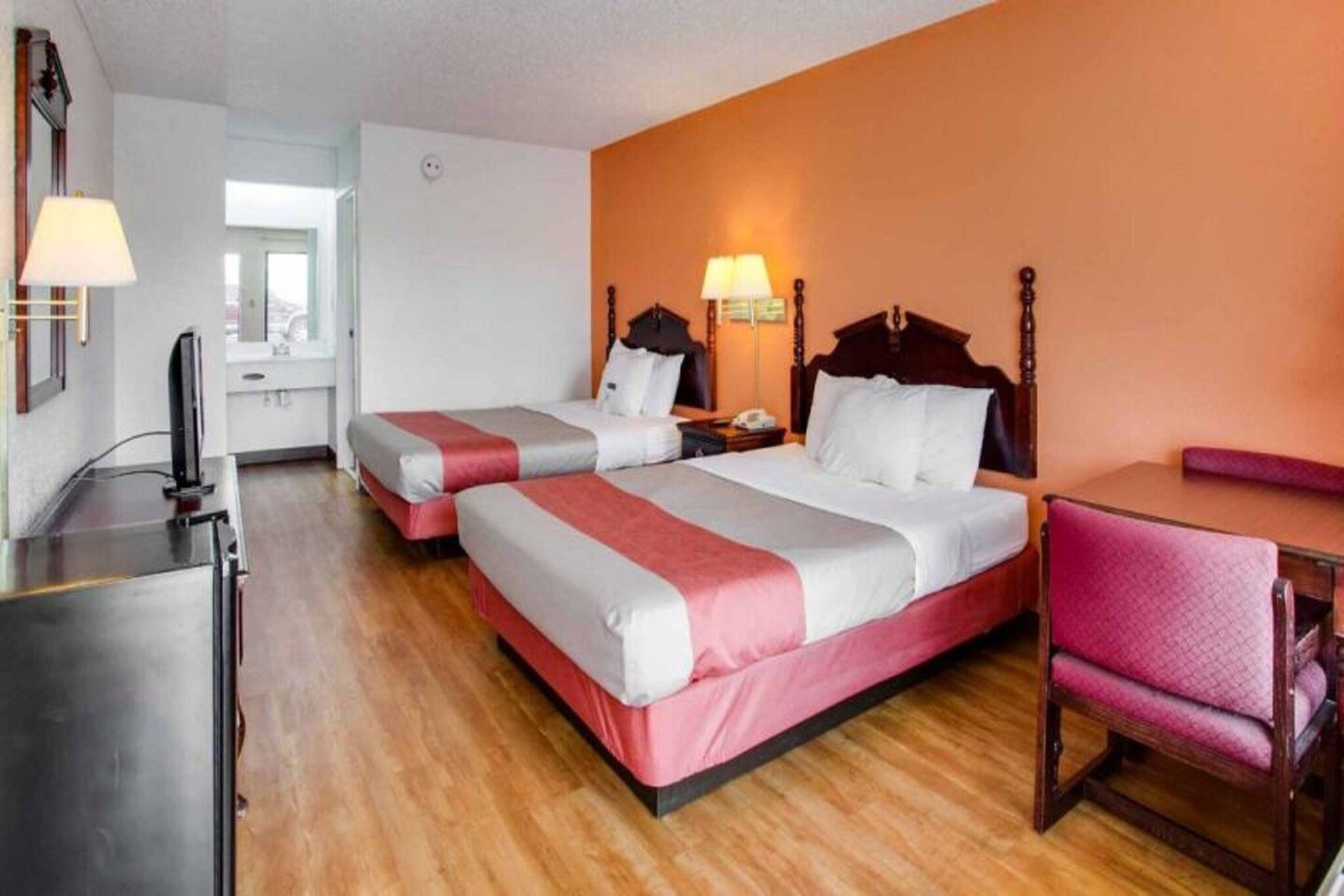 A hotel room with two beds, a desk, a chair, and a television.
