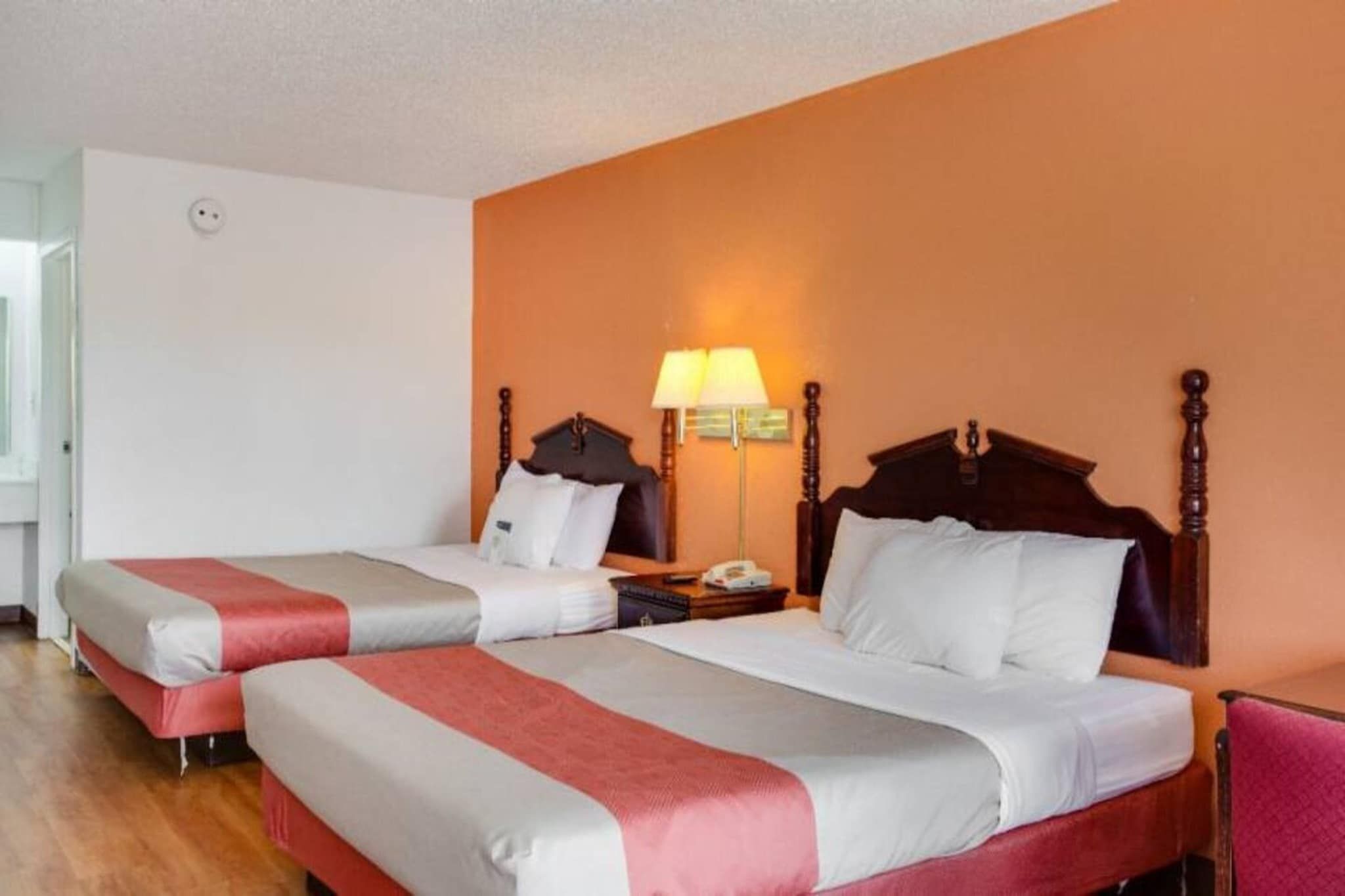 Une chambre d’hôtel avec deux lits, une table de chevet, une lampe et une tête de lit en bois.