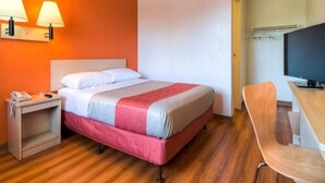 A hotel room with a bed, bedside table, lamp, chair, and a television. - 1 Full Bed | ADA/Tub (Stanton)