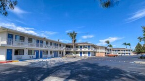 A motel with multiple rooms, a parking lot, and a clear blue sky. - 1 Full Bed | ADA/Tub (Stanton)