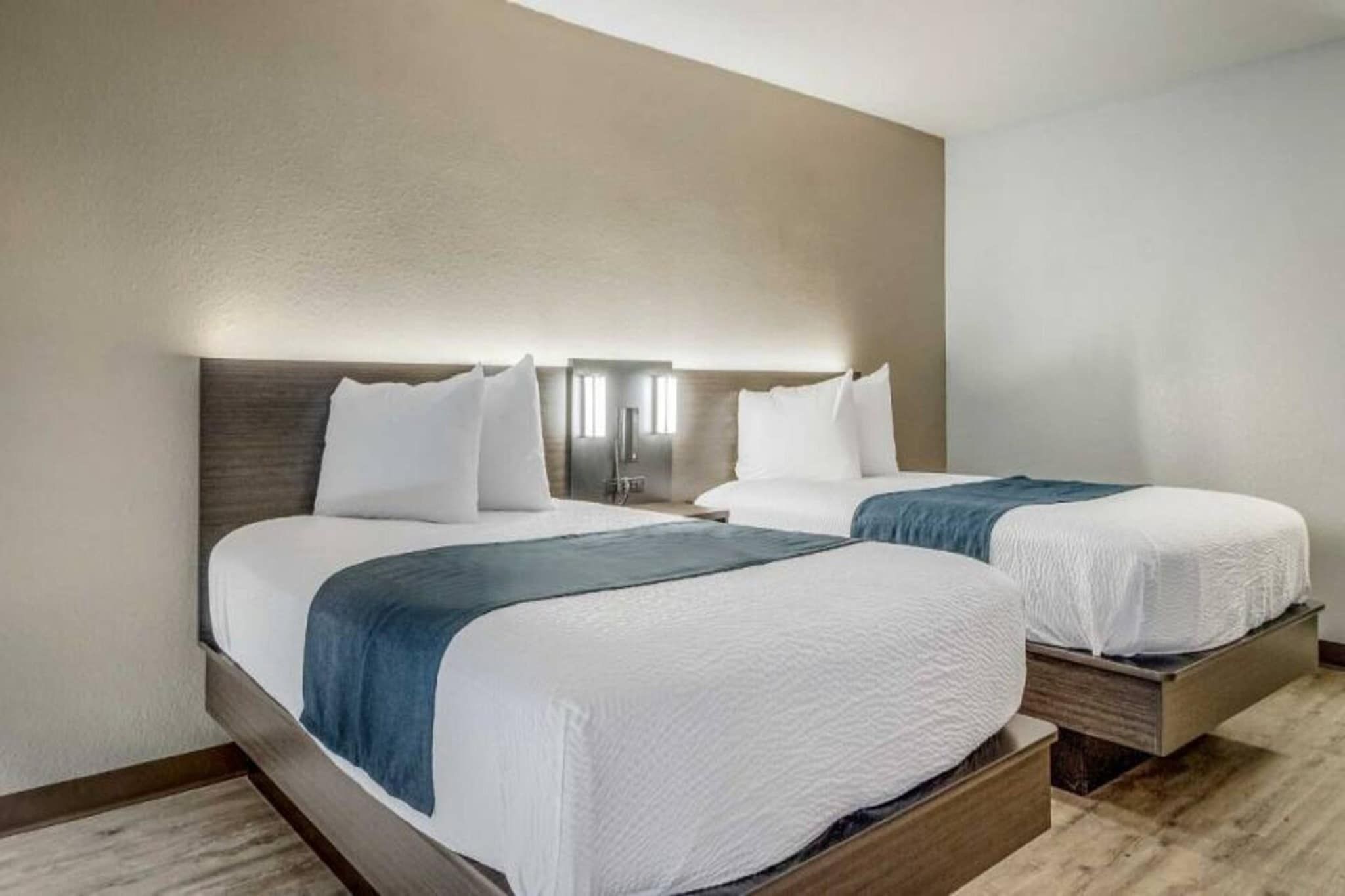 A hotel room with two beds, a wooden headboard, and a nightstand with a lamp.