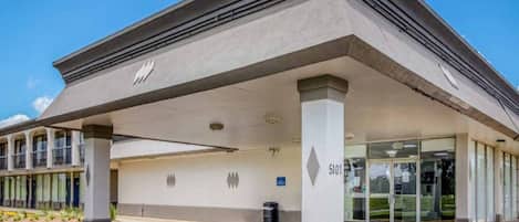 A building with a covered entrance, a clear sky, and a parking lot.
