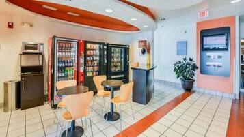 Ein modernes Interieur mit Verkaufsautomaten, einer kleinen Kühlmöglichkeit und einer Sitzecke mit Tischen und Stühlen.