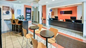 Um hall de hotel com balcão de recepção, área de estar e um quiosque de informação digital.