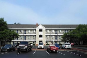 A multi-story hotel with a central entrance, parking lot, and a clear sky. - Spacious Full Beds,Free Parking&TV (Greensboro)