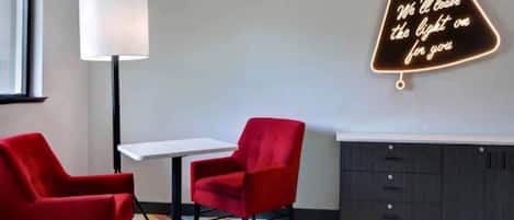 A modern room with a white table, two red chairs, a floor lamp, and a neon sign on the wall.