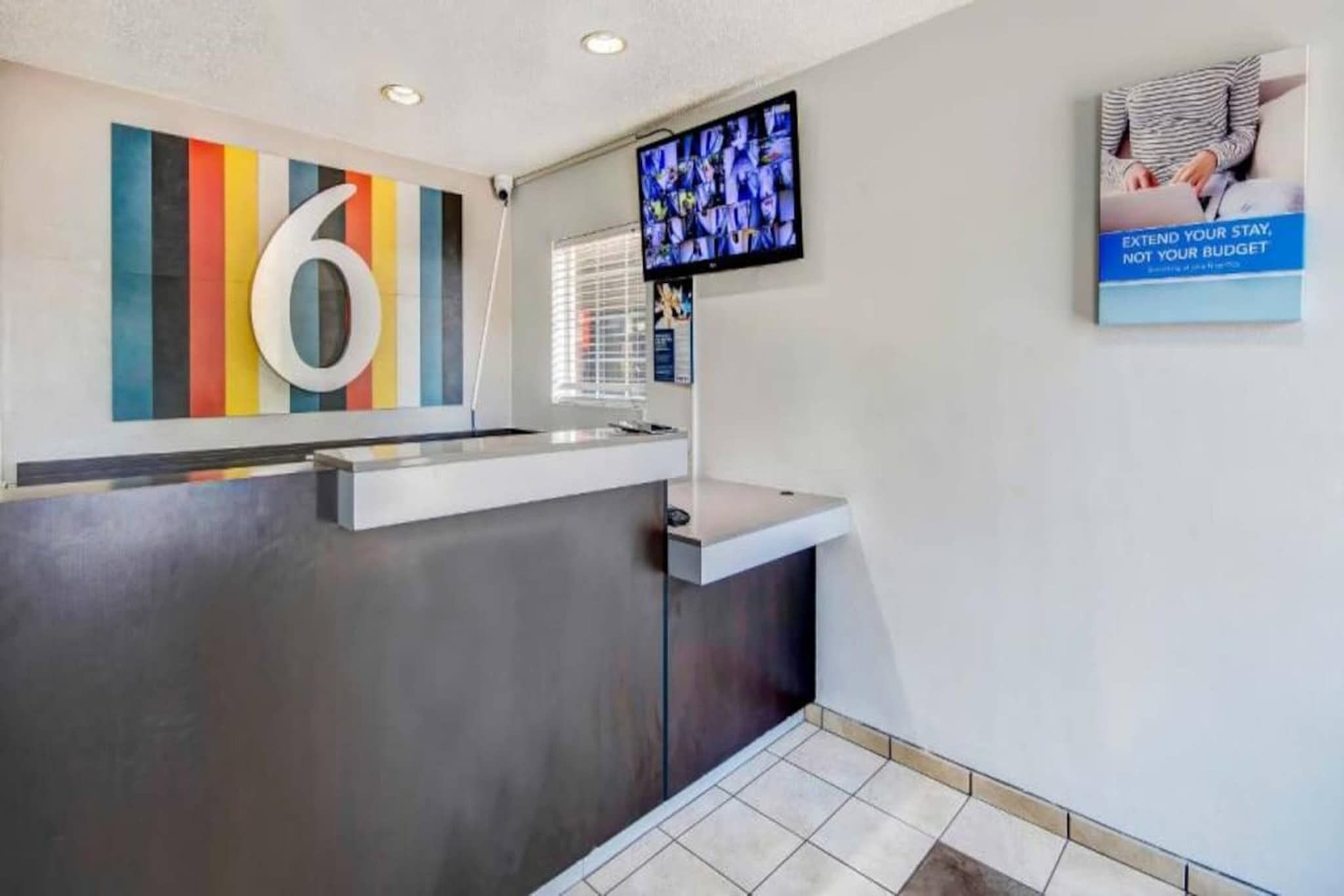 A reception desk with a modern design, a large number '6' on the wall, a television screen, and a poster advertising budget extension.
