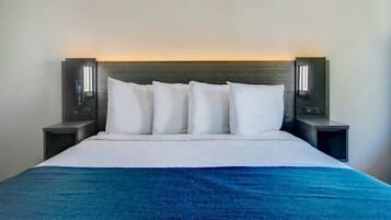 A bed with a white headboard, four white pillows, and a blue throw blanket.