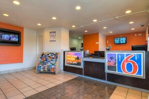 A hotel reception area with a tiled floor, a magazine rack, a digital screen, and a sign for the 6th floor.