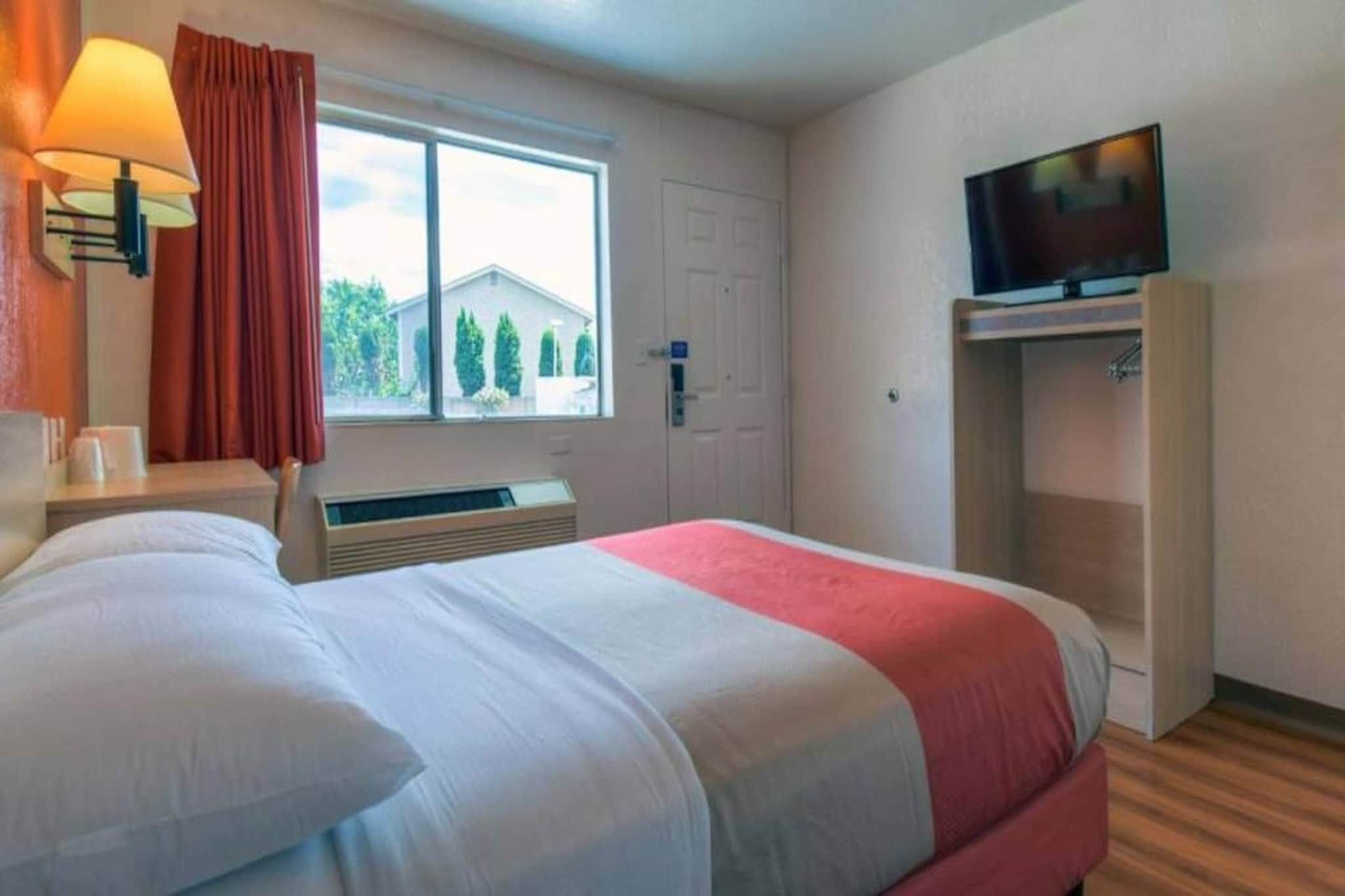 Een hotelkamer met een bed, een televisie, een raam met gordijnen en een verwarming.