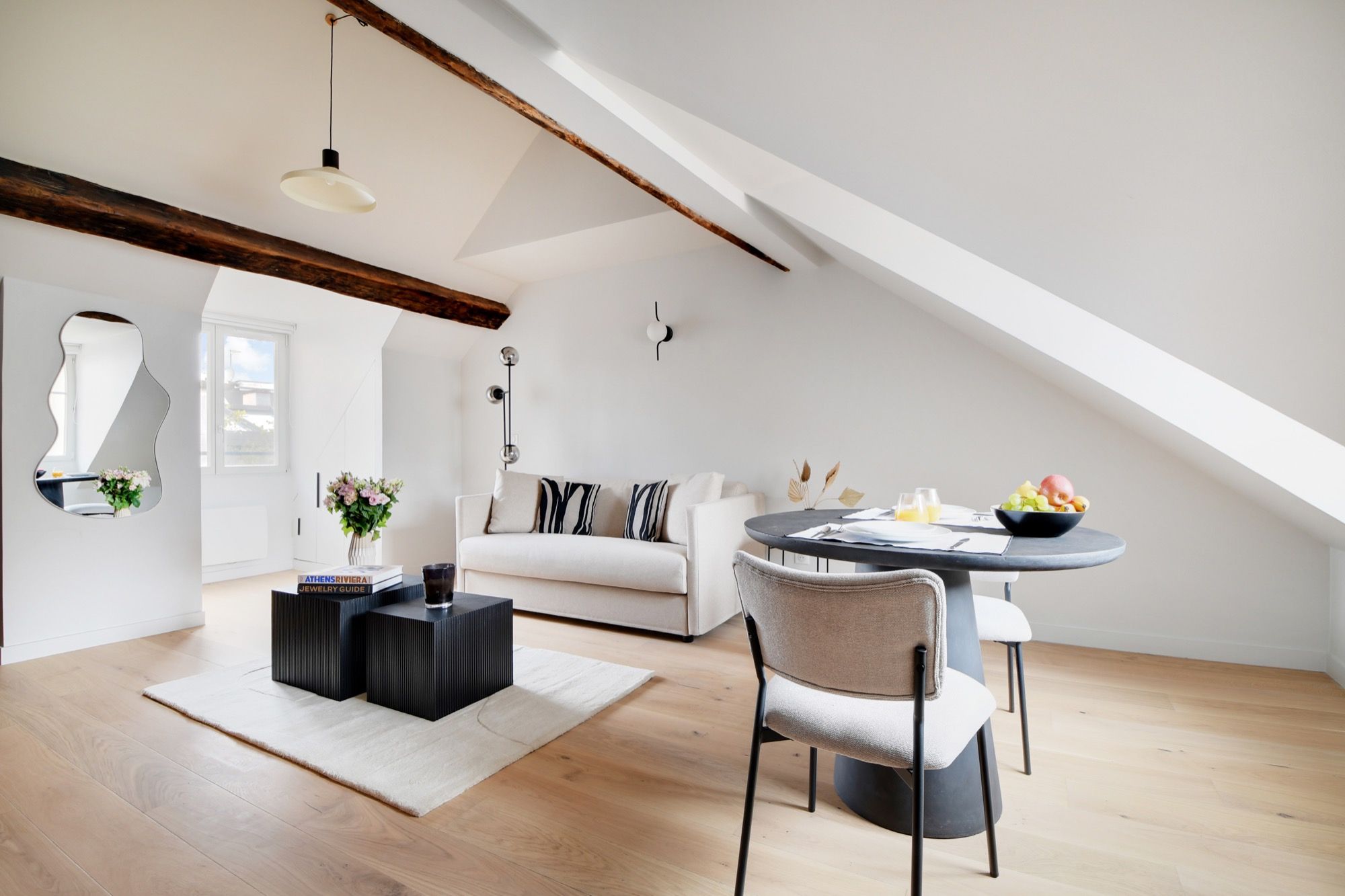 Un loft moderne avec un plafond haut, des poutres apparentes, une table de salle à manger ronde avec des chaises, un canapé et une table basse.