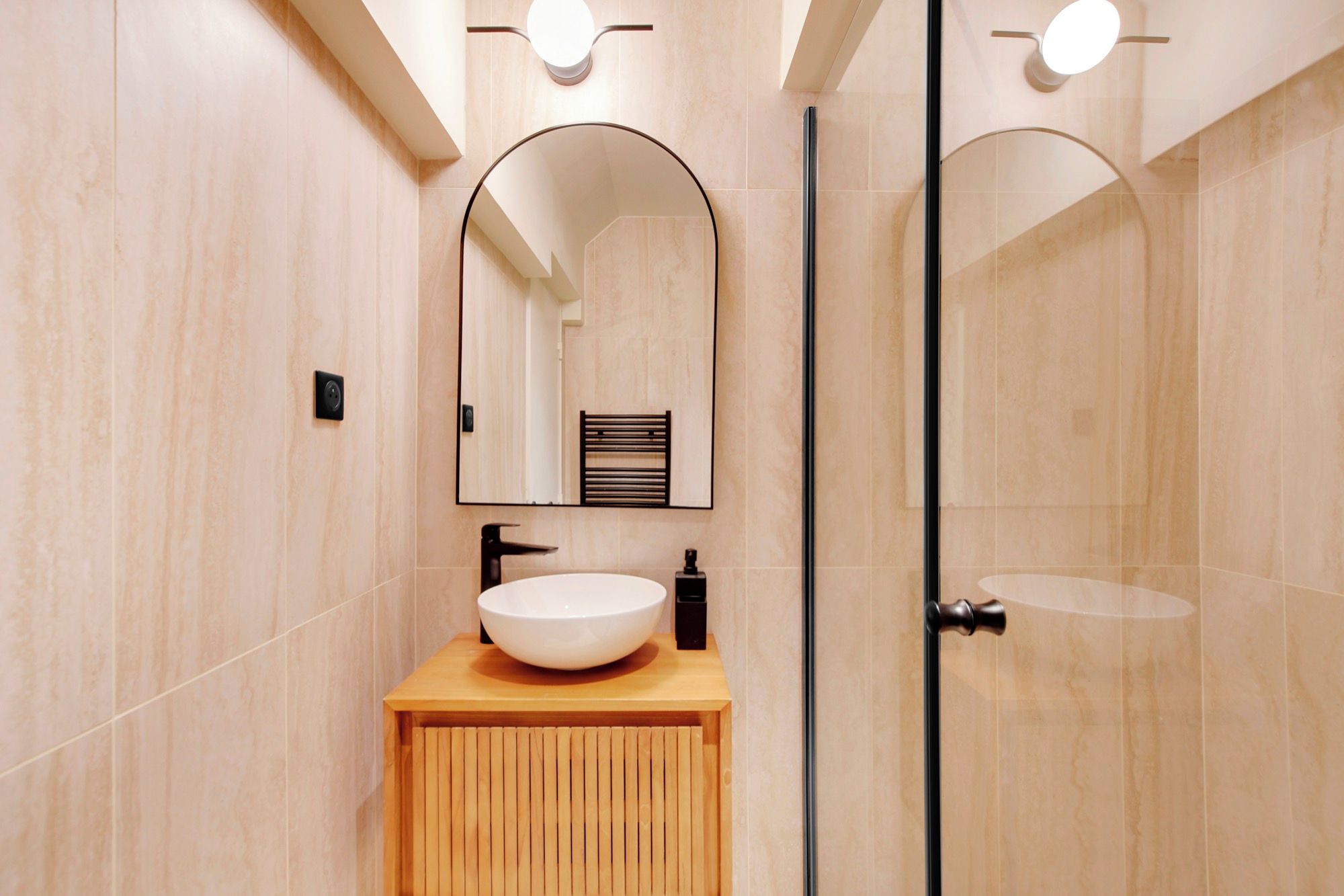 Un baño moderno con un espejo grande, un lavamanos redondo y una cabina de ducha con mampara de vidrio.