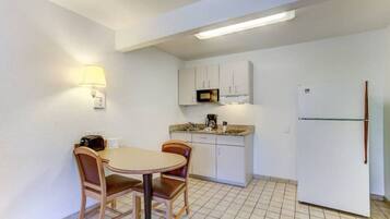 A compact kitchen with a dining table and chairs, a microwave, a refrigerator, and a wall-mounted lamp.