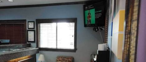 Habitación con barra, ventana con persianas, televisión montada en la pared y una silla estampada.