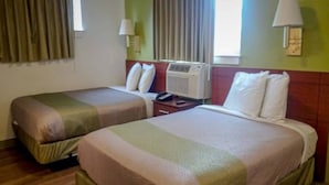 Habitación de hotel con dos camas, una mesita de noche, una lámpara y un equipo de aire acondicionado.
