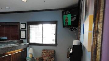 A room with a bar area, a window with blinds, a television mounted on the wall, and a patterned chair.