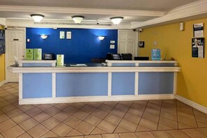 Una recepción con decoración azul y blanca, suelo de baldosas y pared amarilla con carteles informativos.