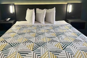 A hotel room with a bed, two bedside tables, and a nightstand with a phone. - Comfy King Bed|Pool,Free Wifi&TV (Huntsville AL)