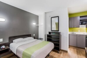 Una camera d'albergo compatta con un letto, un comodino e un angolo cottura.