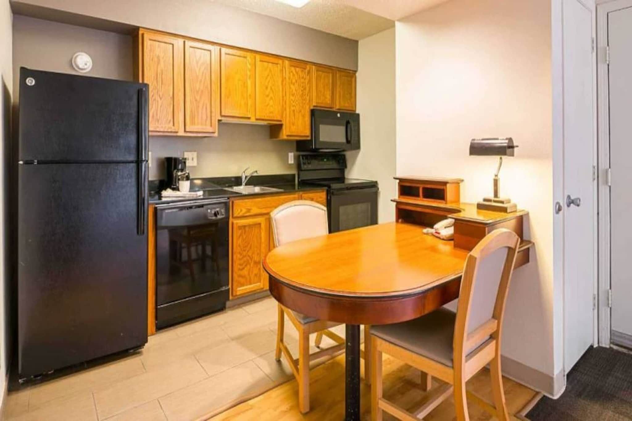 A compact kitchen with wooden cabinets, a black refrigerator, a microwave, and a dining table with chairs.