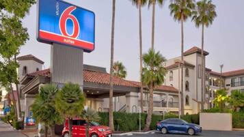 A hotel with a large digital sign advertising '6 suites' and a parking lot with several cars.