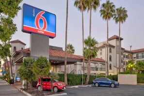 Ein Hotel mit einer großen digitalen Werbetafel, die '6 Suiten' anbietet, und einem Parkplatz mit mehreren Autos.