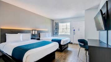 Ein Hotelzimmer mit zwei Betten, einem Schreibtisch, einem Sessel und einem Fernseher.