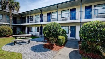 A multi-story motel with a covered parking area, a picnic table, and well-maintained landscaping.