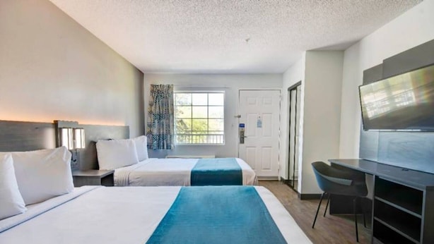 Een hotelkamer met twee bedden, een bureau, een stoel, een televisie en een raam met uitzicht.