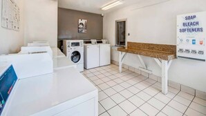 Un cuarto de lavandería con varias lavadoras, un banco y un cartel que enumera jabón, lejía y suavizantes.