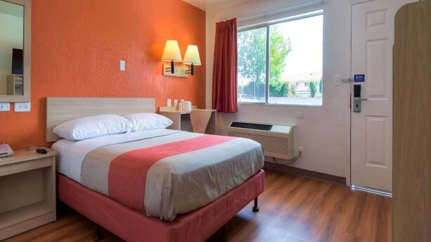 Een hotelkamer met een bed, nachtkastje, lamp, raam en een airconditioner.