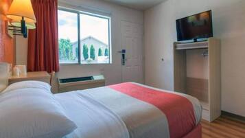 A hotel room with a bed, a television, a window with curtains, and a heater.
