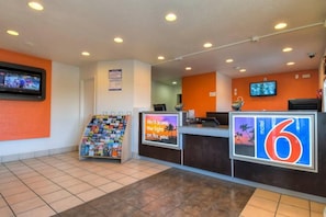 A hotel reception area with a tiled floor, a magazine rack, a digital screen, and a sign for the 6th floor. - 1 Full Bed|ADA/RI Shower (Stanton)