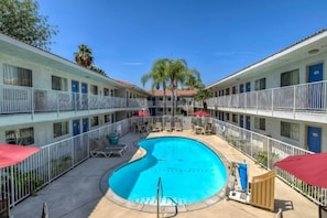 Ein Hotel mit einem zentral gelegenen Schwimmbad, umgeben von Liegestühlen und Sonnenschirmen, mit mehreren Etagen und Balkonen.