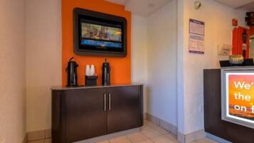 A reception area with a flat-screen TV mounted on the wall, a dark-colored reception desk, and a sign with partially visible text.