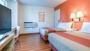 Ett hotellrum med två sängar, ett skrivbord, en tv och en väggmonterad luftkonditioneringsanläggning.