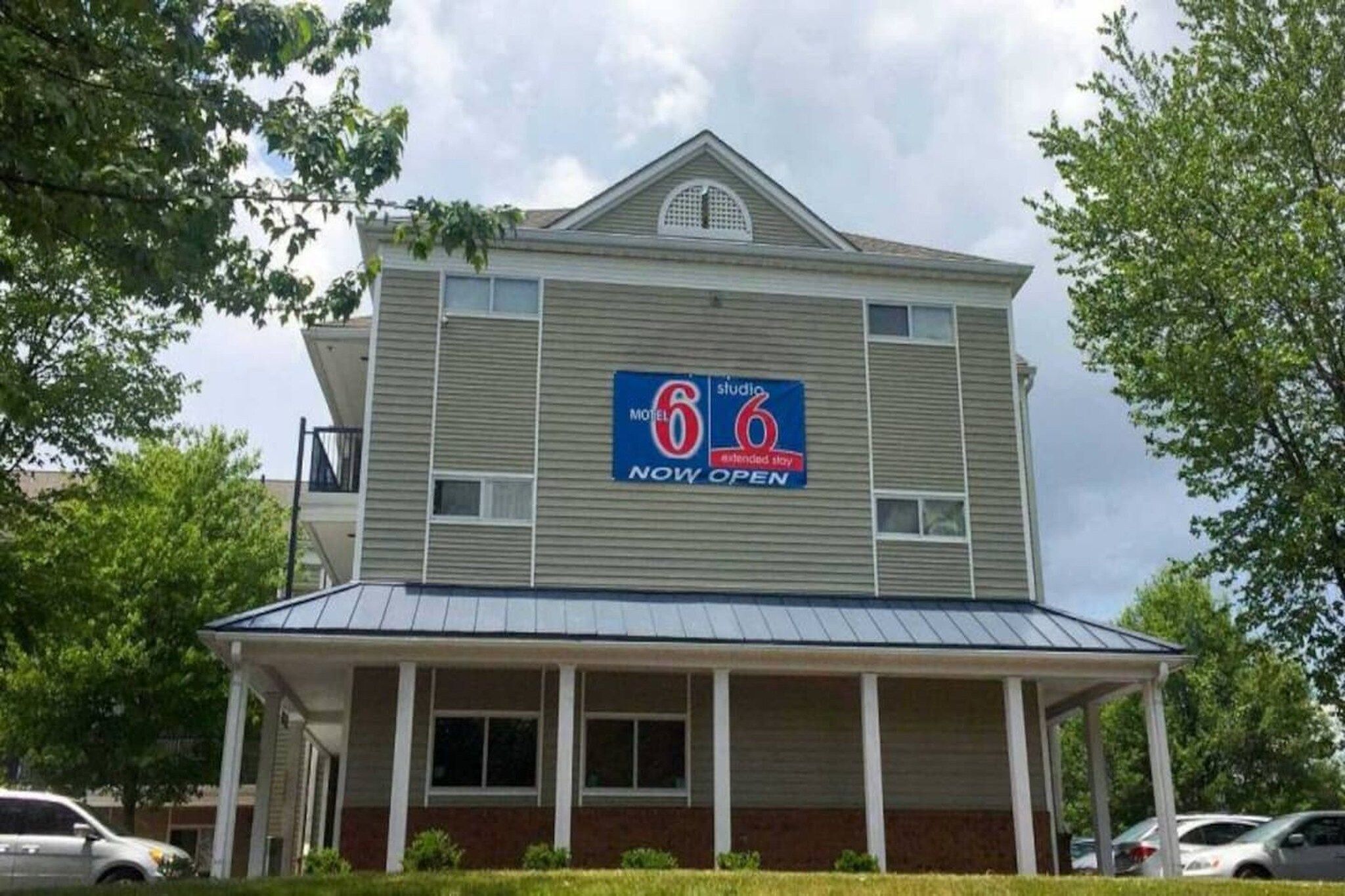 A two-story motel with a '6' logo, a covered front porch, and a 'NOW OPEN' sign.